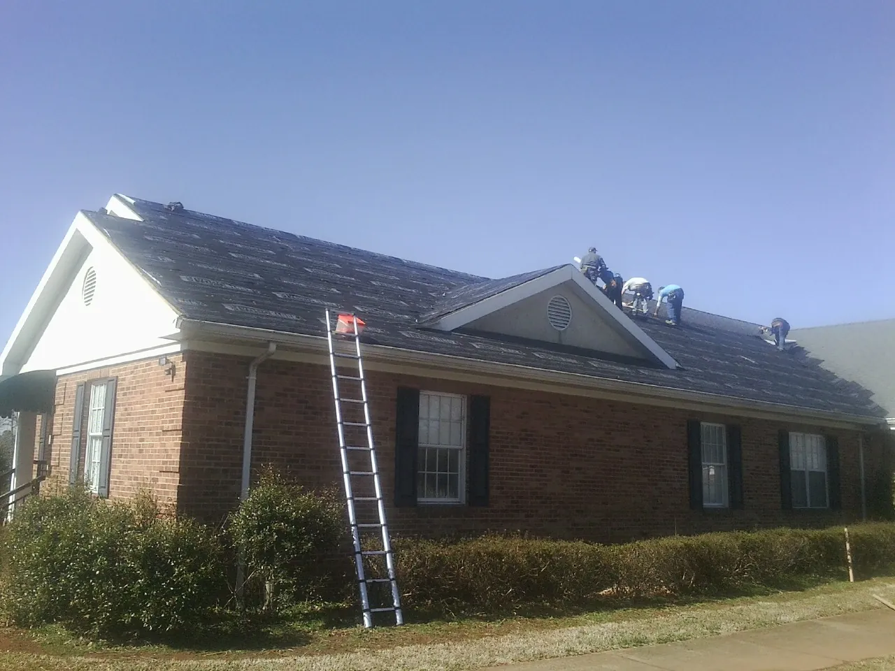 Crew tearing shingles off a brick ranch roof with a ladder set — Metal Roof Repair work by our crew in Lodi