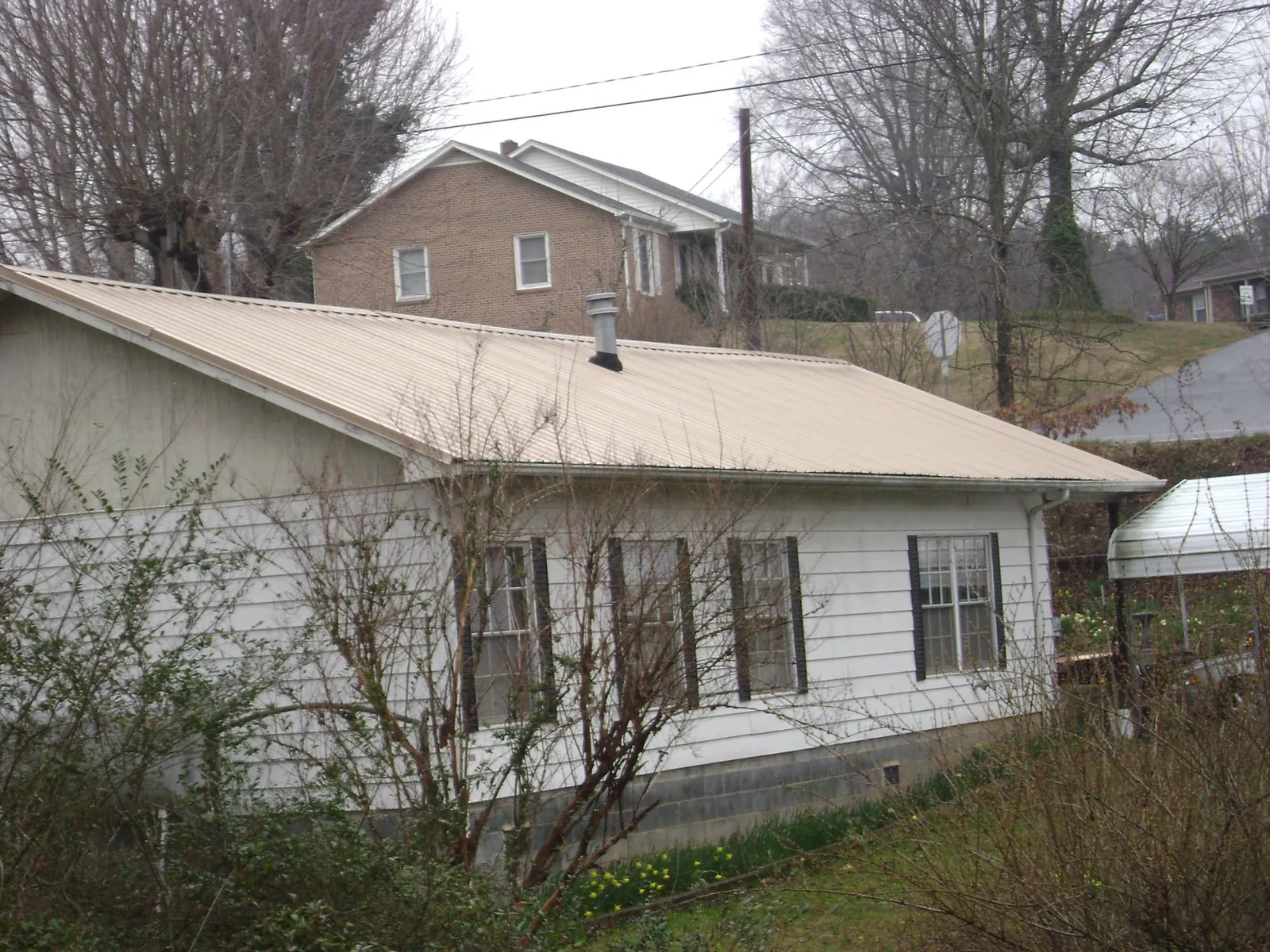 Tan metal roof on a white sided house set into a hillside — Commercial Roofing by Roofing Brothers in Lodi